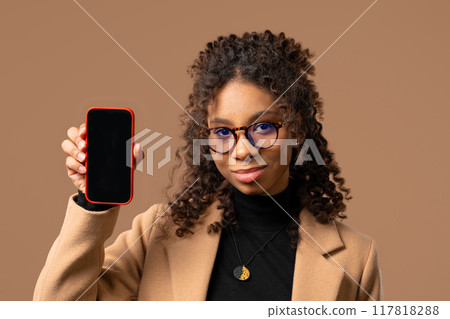 Pretty african teenager girl pointing finger on mobile phone screen on beige 117818288