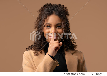 Gossiper african woman with finger on lips - shh, secret, silence, beige studio 117818298