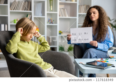 Long-haired young speech therapist working with a blonde boy and both looking involved 117818349