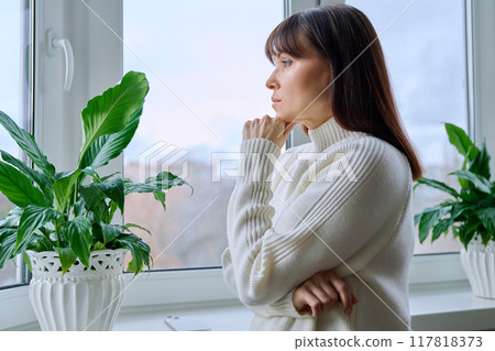 Serious thoughtful middle aged female looking out the window at home Serious thoughtful middle aged female looking out the window at home 117818373