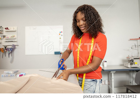 Fashion designer tailor or sewer in workshop cutting textile with scissors Fashion designer tailor or sewer in workshop cutting textile with scissors 117818412
