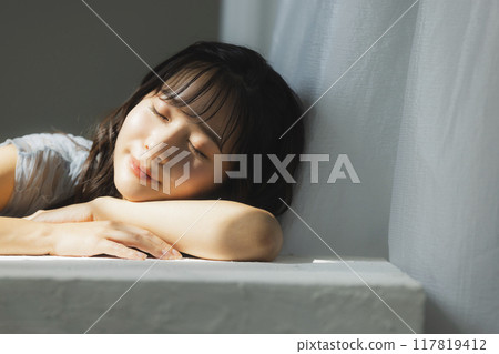 Woman by the window in the setting sun 117819412