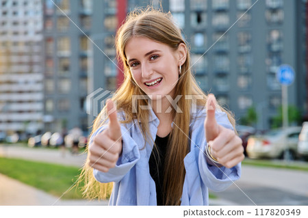 Young happy cheerful woman showing thumbs up, outdoors. 117820349