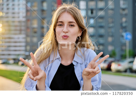 Young beautiful happy cheerful woman showing victory gesture with hands, outdoors. 117820350