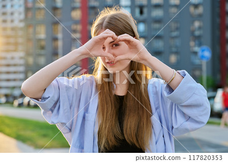 Young happy young woman showing heart with hands, city background Young happy young woman showing heart with hands, city background 117820353