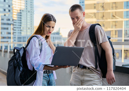 Surprised teenage college age students looking at laptop screen, modern city background 117820404