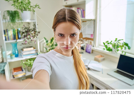 Close-up selfie portrait of teenage serious girl looking at web camera 117820475
