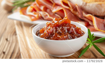 Photorealistic image of a bowl of fig jam next to thinly sliced Parma ham on a rustic wooden board Photorealistic image of a bowl of fig jam next to thinly sliced Parma ham on a rustic wooden board 117821028