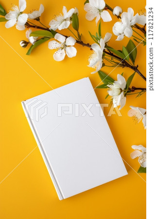 A white book on a vibrant yellow background, adorned with delicate white blossoms A white book on a vibrant yellow background, adorned with delicate white blossoms 117821234