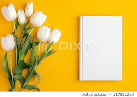 A white book on a vibrant yellow background with white tulips artistically arranged A white book on a vibrant yellow background with white tulips artistically arranged 117821250