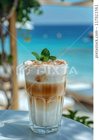 A tall glass of iced coffee topped with whipped cream and mint leaves, set against a serene beach backdrop A tall glass of iced coffee topped with whipped cream and mint leaves, set against a serene beach backdrop 117821561