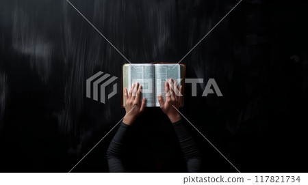 Human hands holding open Bible against black 117821734