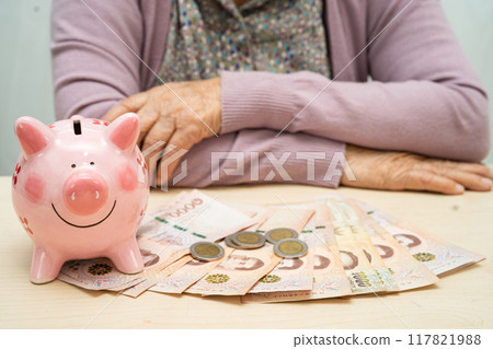 Asian elderly woman with pink piggy bank for saving money and insurance, poverty, financial problem in retirement. Asian elderly woman with pink piggy bank for saving money and insurance, poverty, financial problem in retirement. 117821988