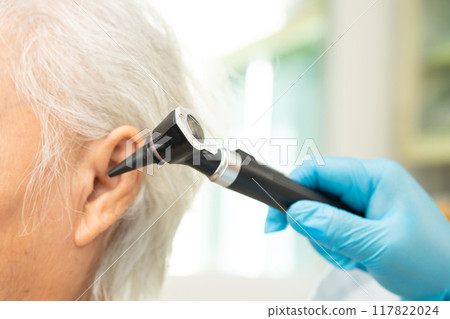 Audiologist use otoscope checking ear of elderly woman patient treating hearing loss problem. Audiologist use otoscope checking ear of elderly woman patient treating hearing loss problem. 117822024