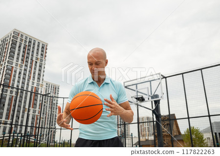 Sporty adult man playing with orange basketball ball on sports court at courtyard. Street style. Team sport. Fun exercise. Sporty adult man playing with orange basketball ball on sports court at courtyard. Street style. Team sport. Fun exercise. 117822263