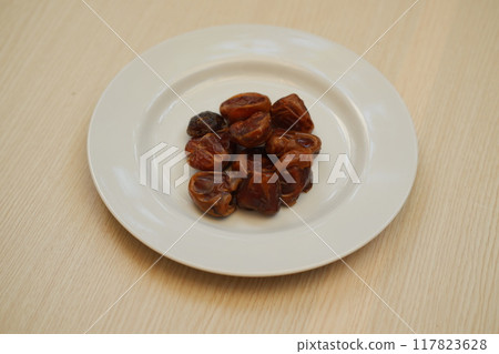 Fresh dates arranged neatly on a white plate, ready to be enjoyed. 117823628