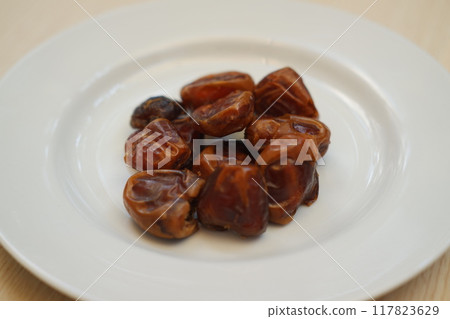 Fresh dates arranged neatly on a white plate, ready to be enjoyed. 117823629