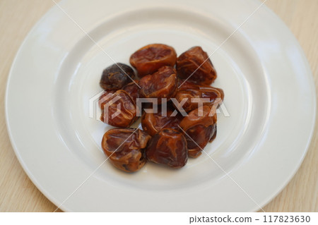 Fresh dates arranged neatly on a white plate, ready to be enjoyed. 117823630