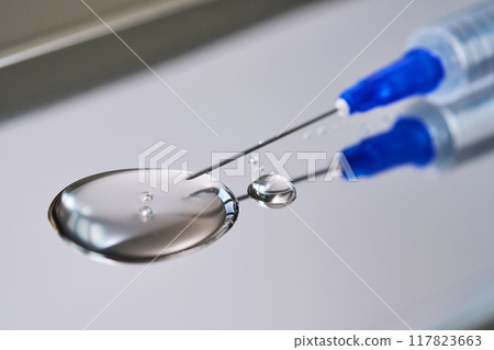 A drop of medicine flowing from a syringe with a needle. 117823663