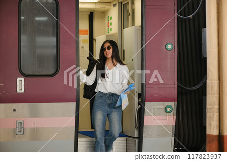A woman is walking out of a train car with a backpack and a blue book A woman is walking out of a train car with a backpack and a blue book 117823937