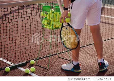 Tennis player holding racket and ball standing near net on court, close up 117824395