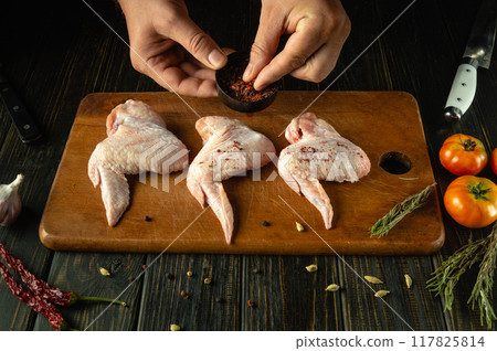 Butcher hands prepares chicken wings for frying with spices. Preparation of cooking Buffalo wings on the kitchen table 117825814
