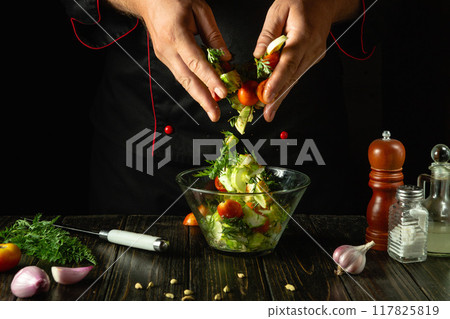 Chef preparing vegetable mix for breakfast. Preparing salad with fresh vegetables on kitchen table. The cook hands mixing chopped vegetables in bowl 117825819