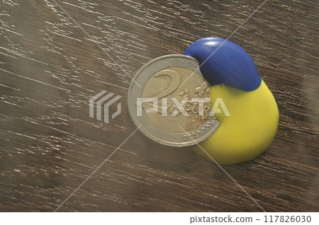 The colors of the Ukrainian flag on the 2 euro coin. Euro coin in fog on dark wooden table 117826030