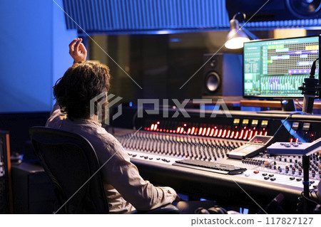 Sound designer counting down for singer in vocal booth to start performance for recording session, producing new music in control room. Skilled audio engineer operating panel board. Sound designer counting down for singer in vocal booth to start performance for recording session, producing new music in control room. Skilled audio engineer operating panel board. 117827127
