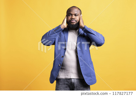 African american man troubled by excessive noise, suppressing it. BIPOC person covering ears with hands, annoyed by loud surrounding sounds, isolated over studio background 117827177
