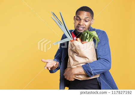 Vegan african american guy gets excited after buying ethically sourced goods, shopping for organic ripe produce from farmers market. Young person carrying paper bag with bio food items. Vegan african american guy gets excited after buying ethically sourced goods, shopping for organic ripe produce from farmers market. Young person carrying paper bag with bio food items. 117827192