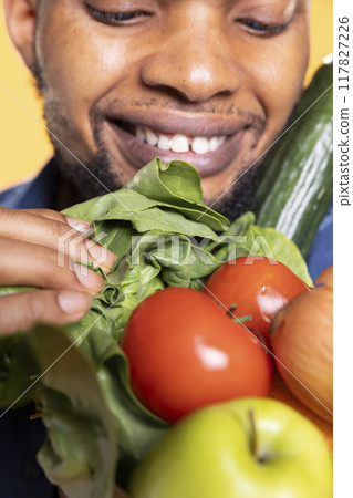 African american man looks at ethically sourced ripe goods in a paper bag, smelling the fresh scent of fruits and veggies in studio. Chef cooking with bio organic ingredients. Close up. African american man looks at ethically sourced ripe goods in a paper bag, smelling the fresh scent of fruits and veggies in studio. Chef cooking with bio organic ingredients. Close up. 117827226
