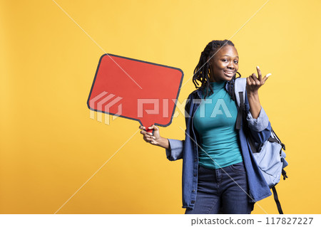 Jolly BIPOC girl holding red speech bubble sign of empty copy space for message. Smiling african american person presenting thought bubble cardboard used as promotion concept, studio background Jolly BIPOC girl holding red speech bubble sign of empty copy space for message. Smiling african american person presenting thought bubble cardboard used as promotion concept, studio background 117827227