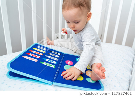 Baby happily plays with felt board in crib 117827401