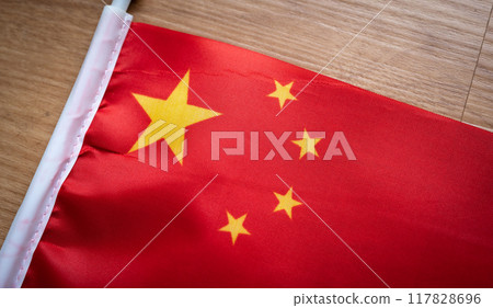 Close up of a flag of China on wooden table. The national flag of the People's Republic of China is red in color, rectangular in shape, with five stars. Close up of a flag of China on wooden table. The national flag of the People's Republic of China is red in color, rectangular in shape, with five stars. 117828696