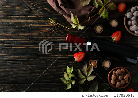 A bottle of wine on a dark, wooden table with flowers. 117829613