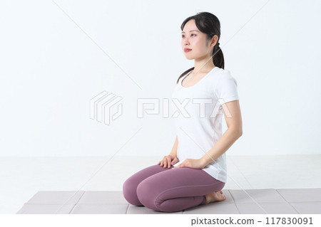 A woman in her twenties sitting upright on a yoga mat 117830091