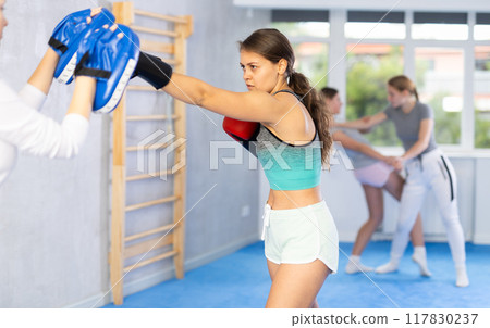 Girls works out strength and speed of boxing punch mitts with help of partner in boxing paws Girls works out strength and speed of boxing punch mitts with help of partner in boxing paws 117830237