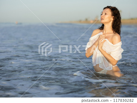 Topless woman in white shirt kneeling on coast Topless woman in white shirt kneeling on coast 117830282