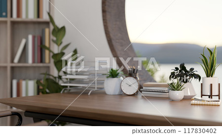 A wooden desk against the window features decorating plants and stationery in a contemporary room. A wooden desk against the window features decorating plants and stationery in a contemporary room. 117830402