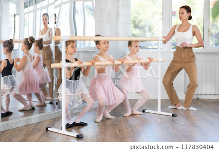 Little girls doing ballet at group training session in the studio performs demi plie near the ballet barre, standing in ballet stance 117830404