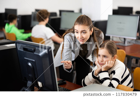 Positive woman teacher together with the girl teaches how to work on computer Positive woman teacher together with the girl teaches how to work on computer 117830479