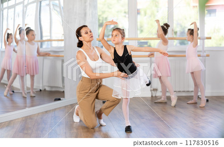 Ballet lesson for little girls - choreography teacher shows little ballerinas how to get into different poses correctly in sturio 117830516