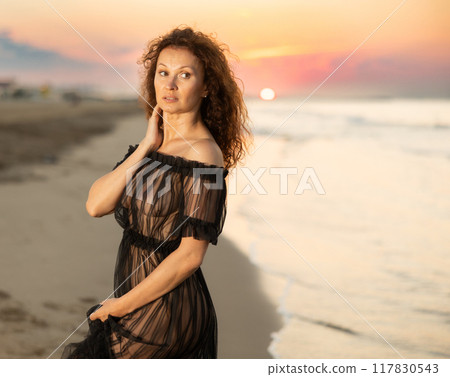 Woman in black negligee stands on coast Woman in black negligee stands on coast 117830543