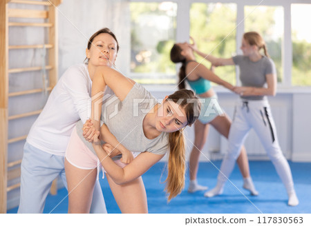 Self defense class - teenage girl, paired with a trainer, learns to deliver painful blows Self defense class - teenage girl, paired with a trainer, learns to deliver painful blows 117830563