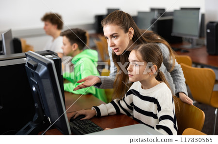 Female teacher helping teen schoolgirl studying in computer lab 117830565