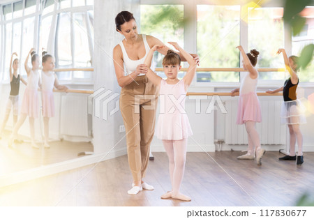 In studio, mentor corrects girls arm and leg, teaches correct dynamics and execution of movements In studio, mentor corrects girls arm and leg, teaches correct dynamics and execution of movements 117830677