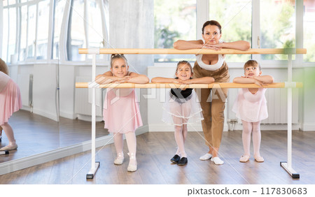 Woman teacher and group of girls posing at barre Woman teacher and group of girls posing at barre 117830683