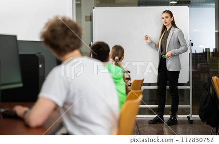 Teacher standing at marker board in computer class in front of pupils Teacher standing at marker board in computer class in front of pupils 117830752