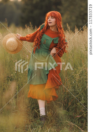 A shepherdess woman with red hair and a green dress sits in a field of flowers. A shepherdess woman with red hair and a green dress sits in a field of flowers. 117833719